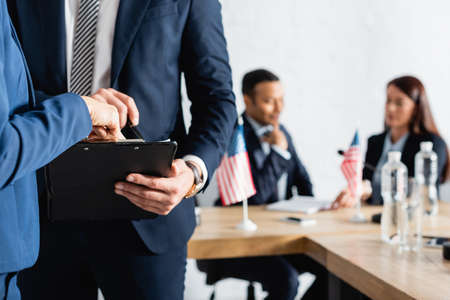 politician pointing with finger at clipboard while colleagues talking on blurred backgroundの写真素材