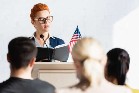political agitator looking at notebook in front of voters in conference room, blurred foregroundの写真素材