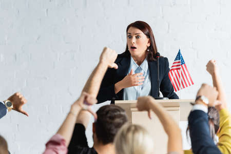 shocked political agitator in front of voters showing thumbs down in conference room, blurred foregroundの写真素材
