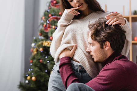 passionate man undressing young woman in sweater near christmas tree on blurred backgroundの写真素材