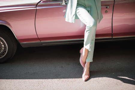 Cropped view of elegant woman standing near retro car on road