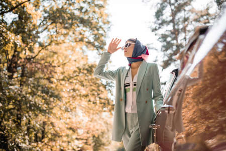Fashionable woman in sunglasses looking away near car outdoors on blurred foreground