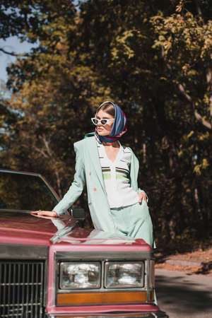 Stylish woman with hand in pocket standing beside vintage car on blurred foregroundの写真素材