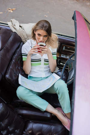 high angle view of young woman with map drinking coffee in vintage cabriolet