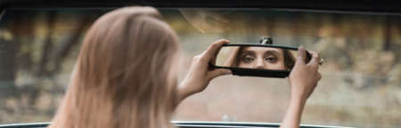 back view of young woman adjusting rearview mirror in car on blurred foreground, bannerの写真素材