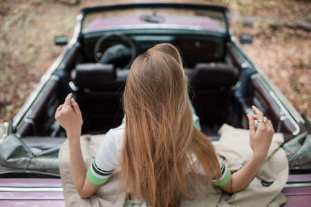 back view of young woman sitting in vintage convertible car on blurred backgroundの写真素材