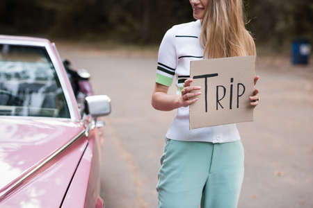 cropped view of woman holding card with trip lettering near cabriolet on blurred background
