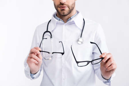 Cropped view of doctor in white coat holding pair of eyeglasses isolated on whiteの写真素材