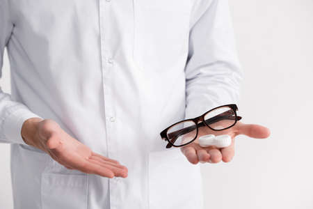 Cropped view of ophthalmologist pointing with hand at eyeglasses and lenses container on palm isolated on whiteの写真素材