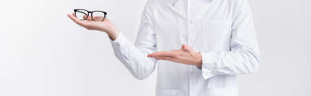 Cropped view of ophthalmologist holding and pointing with hand at eyeglasses on palm isolated on white, bannerの写真素材