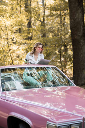 young woman sitting in cabriolet and looking at map in forestの写真素材