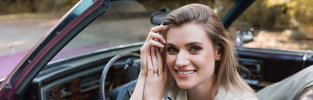 smiling woman holding hands near head while sitting in cabriolet and looking at camera, banner