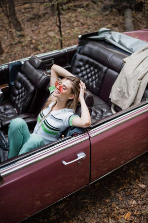 high angle view of joyful woman relaxing while sitting in cabriolet with closed eyes and hands...