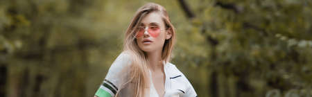 young stylish woman in sunglasses looking away in forest, banner