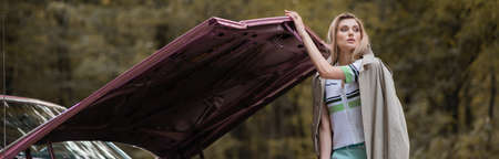 young woman looking away while opening hood of broken vintage car, banner