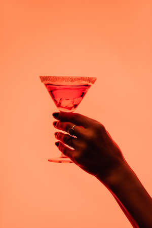 partial view of young woman holding margarita cocktail with ice cubes on orangeの写真素材