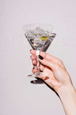 cropped view of woman shaking glass of martini with olive near drops of alcohol on whiteの写真素材