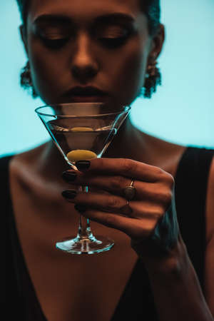 glass of martini with olive in hand of woman on blurred background isolated on blueの写真素材