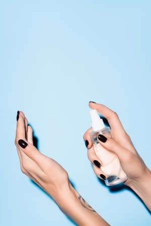 cropped view of young woman using hand sanitizer spray on blueの写真素材