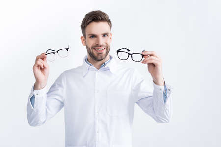 Front view of smiling ophthalmologist showing pair of eyeglasses, while looking at camera isolated...