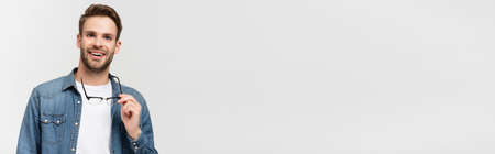 Young man smiling while holding eyeglasses isolated on gray, bannerの写真素材