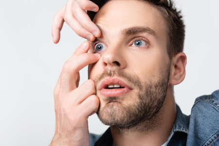 Young man putting contact lens in eye isolated on grayの写真素材