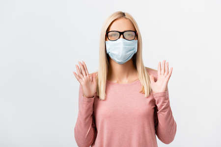 Young woman in misted eyeglasses and medical mask standing isolated on gray