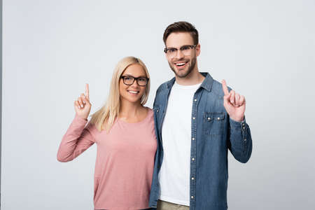 Smiling couple in eyeglasses pointing with fingers isolated on grayの写真素材