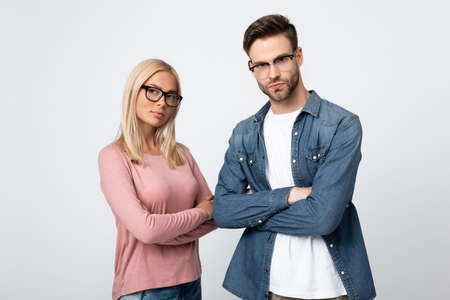 Young couple in eyeglasses looking at camera while standing with crossed arms isolated on grayの写真素材
