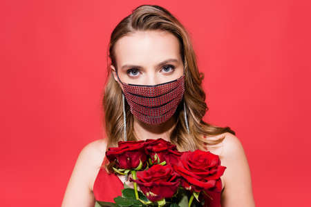 young woman in protective mask near roses with rhinestones looking at camera on redの写真素材