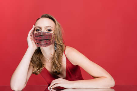 young woman in protective mask with rhinestones looking at camera on redの写真素材