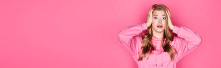 shocked beautiful young woman in hoodie holding head on pink background, bannerの写真素材