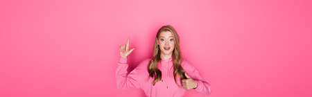 smiling beautiful woman pointing with finger and showing thumb up on pink background, bannerの写真素材