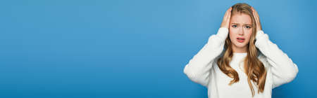 blonde beautiful woman in sweater having headache isolated on blue background, banner
