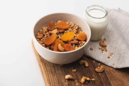 delicious granola with nuts, dried apricots and yogurt on wooden board on white backgroundの写真素材