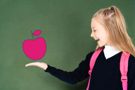 schoolgirl pointing with hand at illustrated pink apple on green chalkboardの写真素材