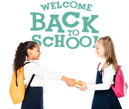 side view of african american schoolgirl giving books to smiling friend isolated on white, welcome...