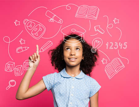 curly african american kid pointing with finger and looking up near illustration on pink