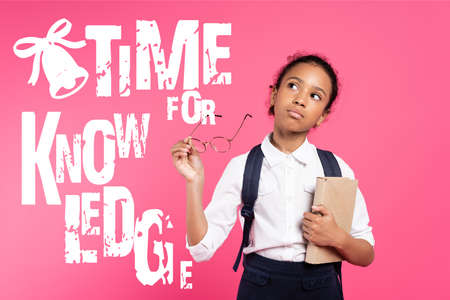 pensive african american schoolgirl with book and eyeglasses standing near time for knowledge...
