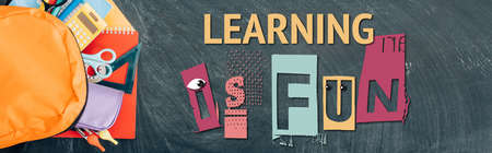 horizontal image of backpack with multicolored school supplies on black chalkboard with learning is fun lettering, top viewの写真素材