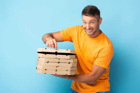 smiling man in t-shirt holding carton pizza boxes on blueの写真素材