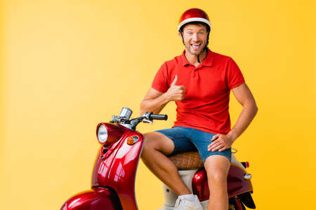 happy man in helmet sitting on red scooter and showing thumb up on yellow