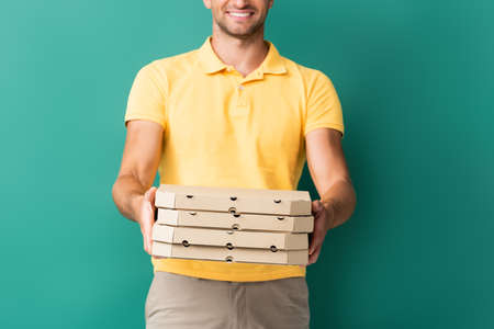 cropped view of cheerful delivery man with outstretched hands holding pizza boxes on blueの写真素材