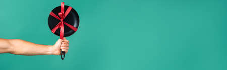 cropped view of man holding new frying pan with red ribbon on turquoise background, bannerの写真素材