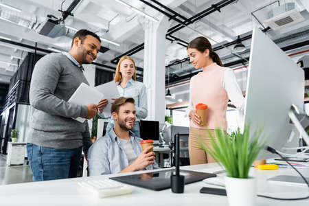 Smiling multicultural businesspeople with devices and coffee to go talking in office