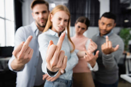 Multicultural businesspeople on blurred background showing middle fingers in officeの写真素材
