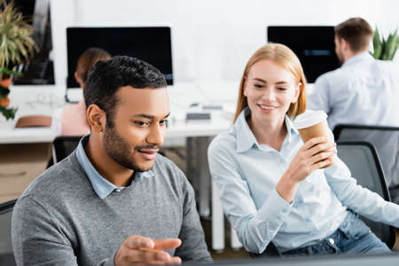 Indian businessman sitting near smiling colleague with coffee to go in officeの写真素材
