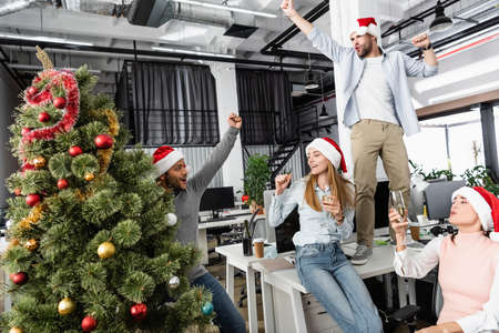 Excited multiethnic businesspeople with champagne and christmas tree celebrating new year in officeの写真素材