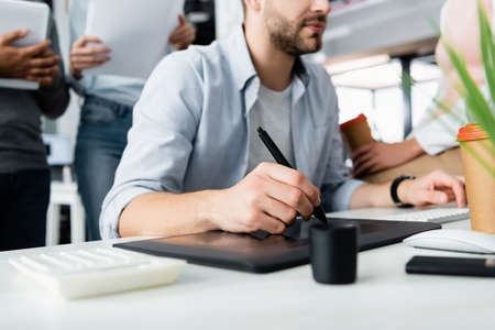 Cropped view of businessman using graphics tablet and computer keyboard near colleagues in office