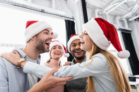 Smiling multiethnic businesspeople embracing while celebrating christmas in officeの写真素材